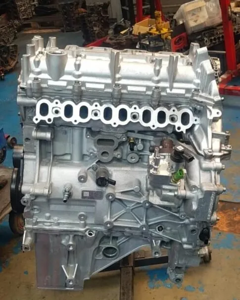 A clean, rebuilt four-cylinder engine block and cylinder head on a workshop stand, with its inlet ports open