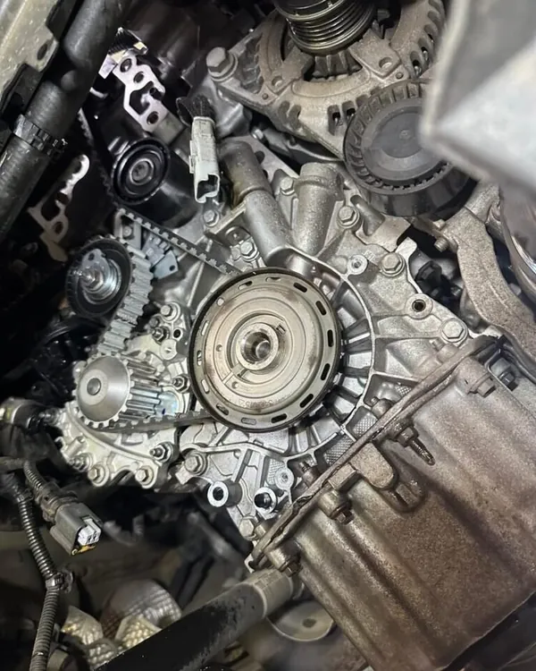 Front of an engine with the timing covers removed, showing the toothed timing belt, its sprockets and tensioner, with the alternator above