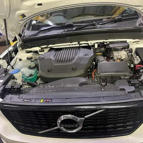 White Volvo with its bonnet raised and the engine bay open, parked in a workshop